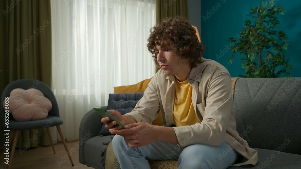 Young man sitting on the sofa in the room and reading news on his smartphone Young man sitting on the sofa in the room and reading news on his smartphone