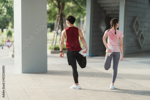 Behind young couple in sportswear doing stretching together before jogging exercise in urban area. Warming up for workout outdoor in the morning.