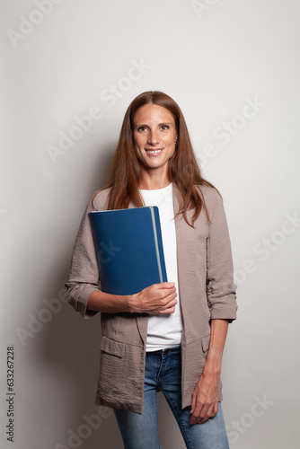Friendly brunette woman smiling, holding blue folder and standing on white background