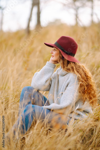 Happy woman with stylish sweater and hat outdoors in autumn park. Woman enjoys autumn nature. Concept of vacation, travel, freedom.