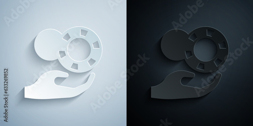 Paper cut Hand holding casino chips icon isolated on grey and black background. Casino gambling. Paper art style. Vector