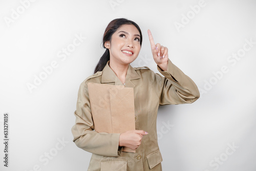 A Young beautiful Asian worker with brown uniform bringing document and pointing to copy space above her. Indonesian PNS.