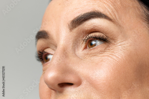 Cropped portarit of beautiful middle-aged woman with healthy, natural condition skin looking away over grey studio background.