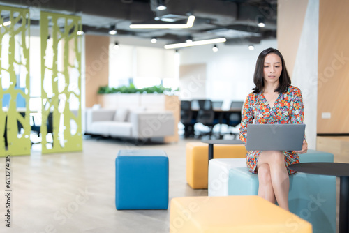 Wide angle shot of Asian female executives Head of the company business department like an employee Sit in a chair and work with a laptop in the office wearing a beautiful floral suit.