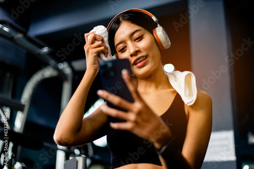 Asian woman wearing fitness clothes Play on the phone, wear white headphones, listen to music, relax during exercise, generate energy for exercise inspiration.