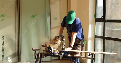 Man is working with miter saw and cutting wooden board. Professional uses material handling equipment for home renovation photo
