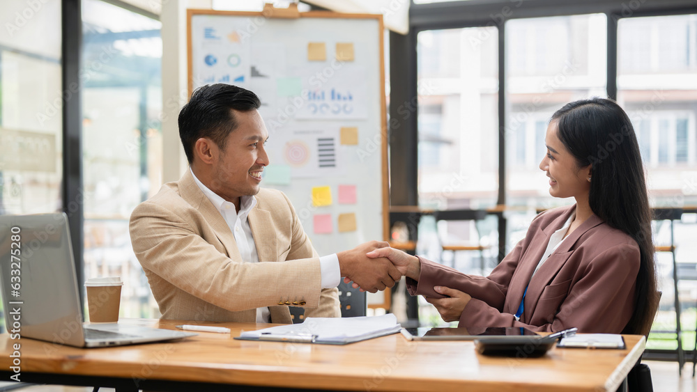 A professional Asian businessman is shaking hands with a female colleague at a table A professional Asian businessman is shaking hands with a female colleague at a table