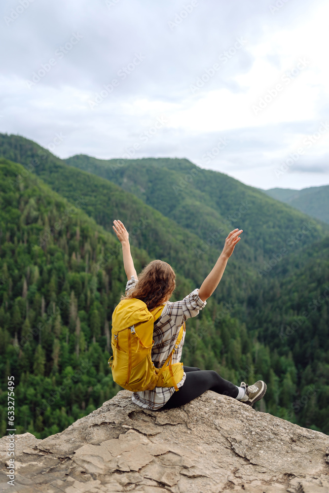 Naklejka premium Beautiful woman with backpack admires view from top of mountain. Mountain tourism. Girl traveler on background of mountains. Active lifestyle.