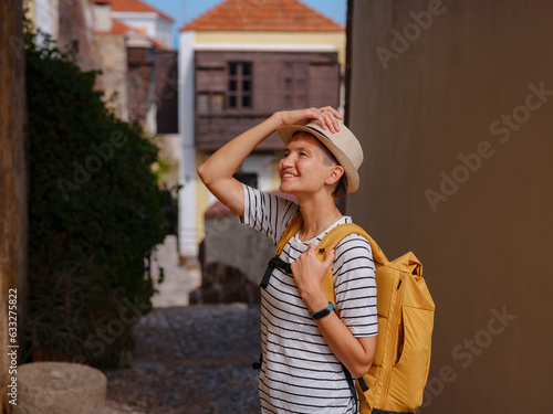 summer trip to Rhodes island Greece. Young Asian woman in striped tshirt and hat walks Street of Knights of Fortifications castle. female traveler visiting southern Europe. Unesco world heritage site