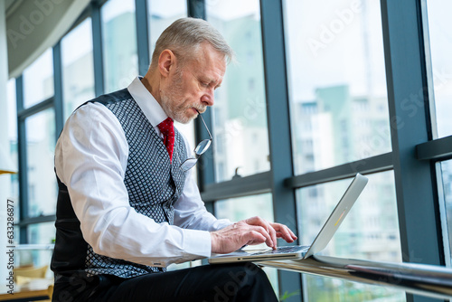 Professional man working on a laptop in a formal setting. A man in a vest and tie using a laptop