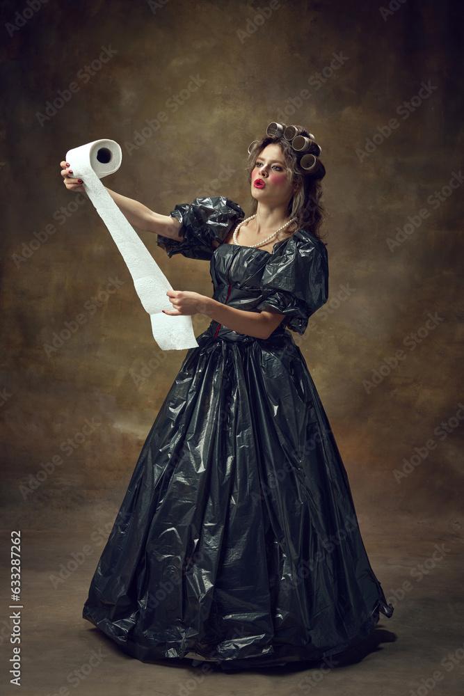 Full lenght portrait of woman wearing in black dress made of garbage bags curls hair with paper tubes reading from disposable towels. Full lenght portrait of woman wearing in black dress made of garbage bags curls hair with paper tubes reading from disposable towels.