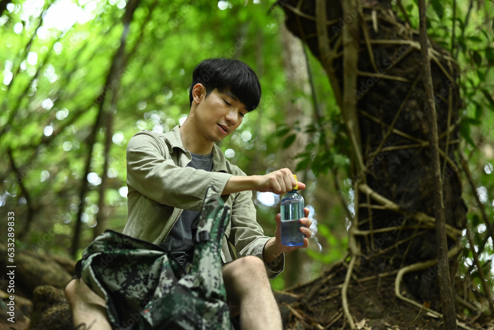 Man traveler taking break in the forest, drinking the water from bottle. Traveling, trekking and adventure concept