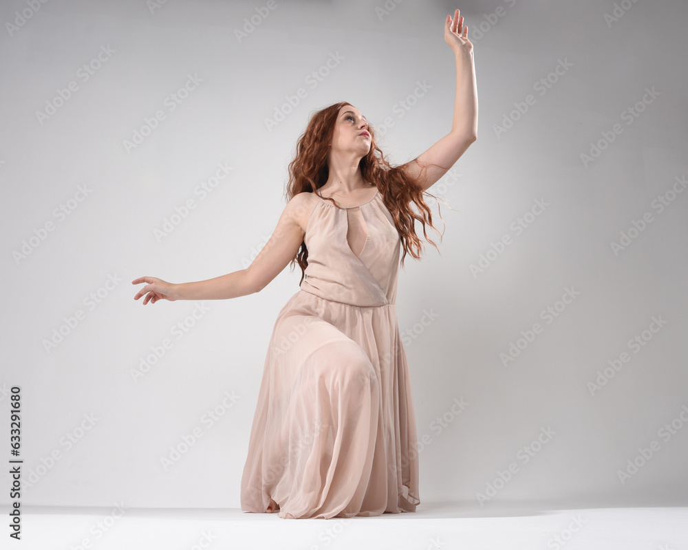Full length portrait of beautiful brunette model wearing a pink dress. graceful sitting pose, kneeling on floor gestural hands. shot from low angle perspective, isolated on white studio background Full length portrait of beautiful brunette model wearing a pink dress. graceful sitting pose, kneeling on floor gestural hands. shot from low angle perspective, isolated on white studio background