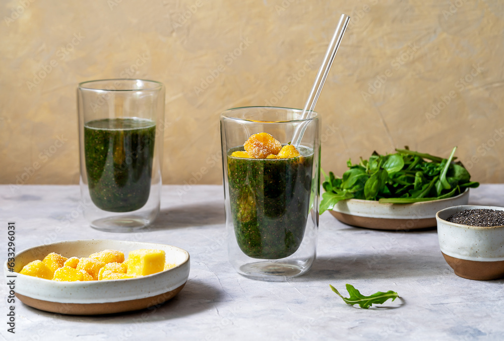 Green smoothie in glasses made with greens, frozen mango, and chia seeds, grey and yellow background, ingredients Green smoothie in glasses made with greens, frozen mango, and chia seeds, grey and yellow background, ingredients