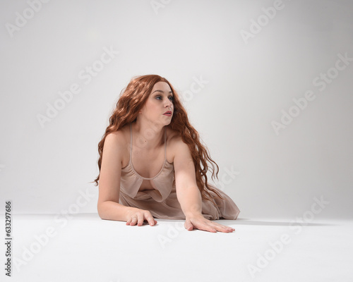 Full length portrait of beautiful brunette model  wearing a  pink dress. graceful sitting  pose  kneeling on floor gestural hands. shot from low angle perspective   isolated on white studio background