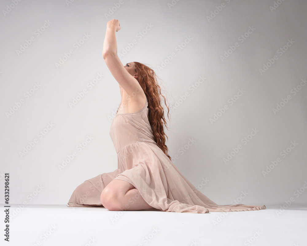 Obraz premium Full length portrait of beautiful brunette model wearing a pink dress. graceful sitting pose, kneeling on floor gestural hands. shot from low angle perspective, isolated on white studio background