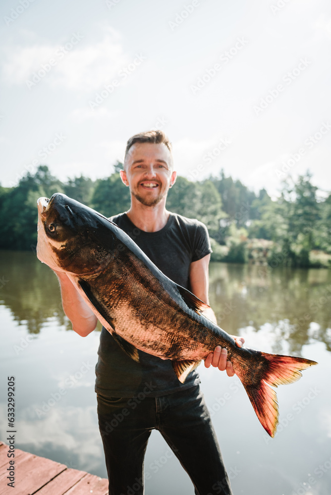 Fresh fish trophy in hands. Young man returning with freshly caught fish. Article about fishing day. Closeup. Fishing backgrounds. Happy fisherman hold big trophy fish near lake. Success pike fishing. Fresh fish trophy in hands. Young man returning with freshly caught fish. Article about fishing day. Closeup. Fishing backgrounds. Happy fisherman hold big trophy fish near lake. Success pike fishing.