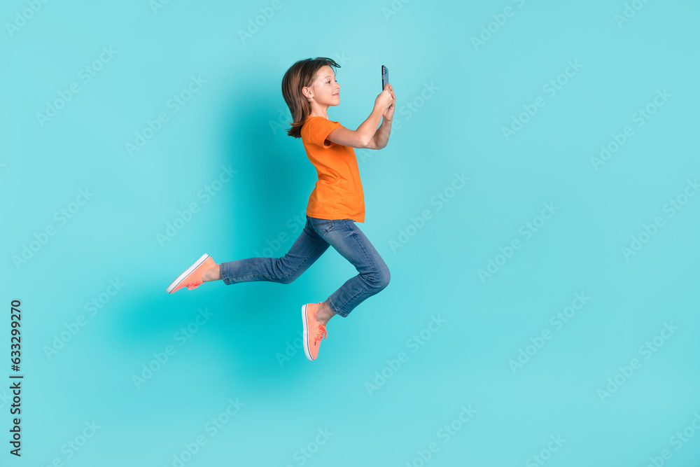 Photo of charming positive girl wear stylish orange clothes fly air use phone photographing selfie isolated on cyan color background