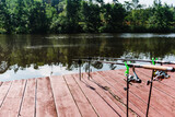 Fishing background. Article about fishing day. Carp, grass carp, crucian carp. Fishing rods, spinning reels on pier. Sunlight against backdrop of lake. Wild nature. Concept of rural getaway.