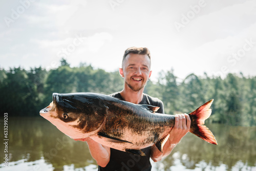 Fresh fish trophy in hands. Young man returning with freshly caught fish. Article about fishing day. Closeup. Fishing backgrounds. Happy fisherman hold big trophy fish near lake. Success pike fishing.