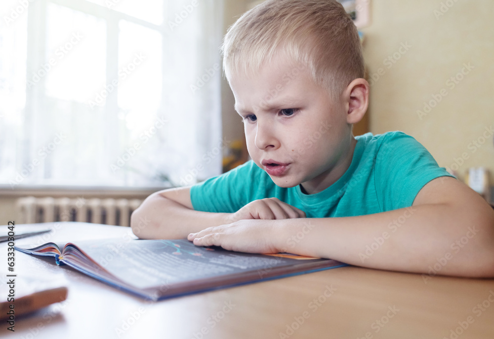 Boy in library. Seven year Ukrainian guy is sitting at a table in library and reading book. Concept of normal learning, thirst for knowledge, desire to learn new things. Blurred background and letters Boy in library. Seven year Ukrainian guy is sitting at a table in library and reading book. Concept of normal learning, thirst for knowledge, desire to learn new things. Blurred background and letters
