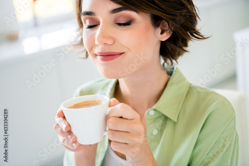 Photo of cute dreamy lady dressed green shirt closed eyes drinking morning americano indoors house kitchen