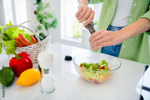 Croped photo of lady dressed green shirt adding hot chilly pepper fresh salad indoors house kitchen