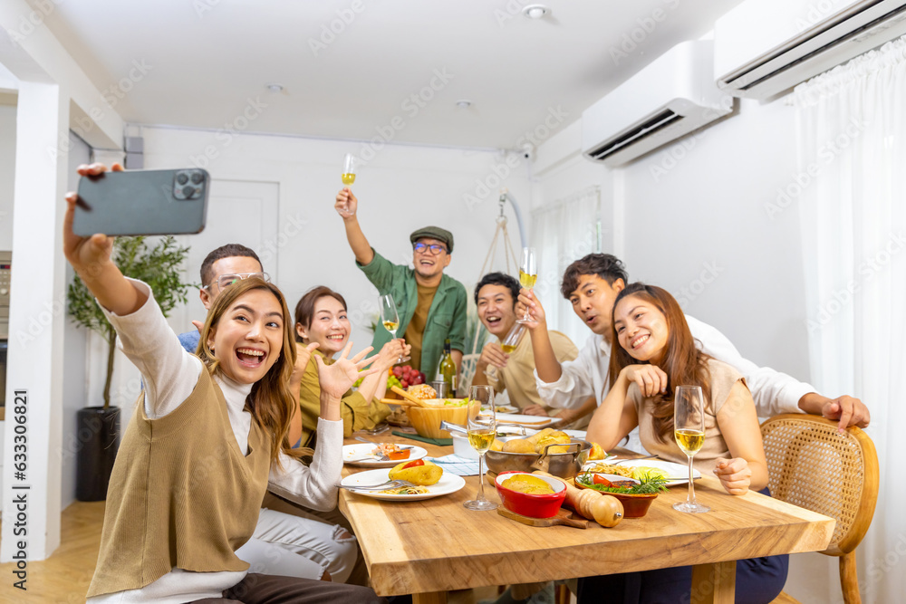 Group of Cheerful Asian man and woman using mobile phone taking selfie together during celebration dinner party at home. Happy people friends enjoy and fun reunion meeting holiday event on vacation. - obrazy, fototapety, plakaty 