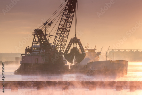Fotografia Grab dredger near the barge dumps soil from the bottom of the sea onto the barge