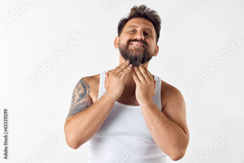 Handsome, mature, bearded man taking care after beard with cosmetics, applying gel, wax, oil against white studio background. Concept of men's beauty, skin care, cosmetology, health and wellness.