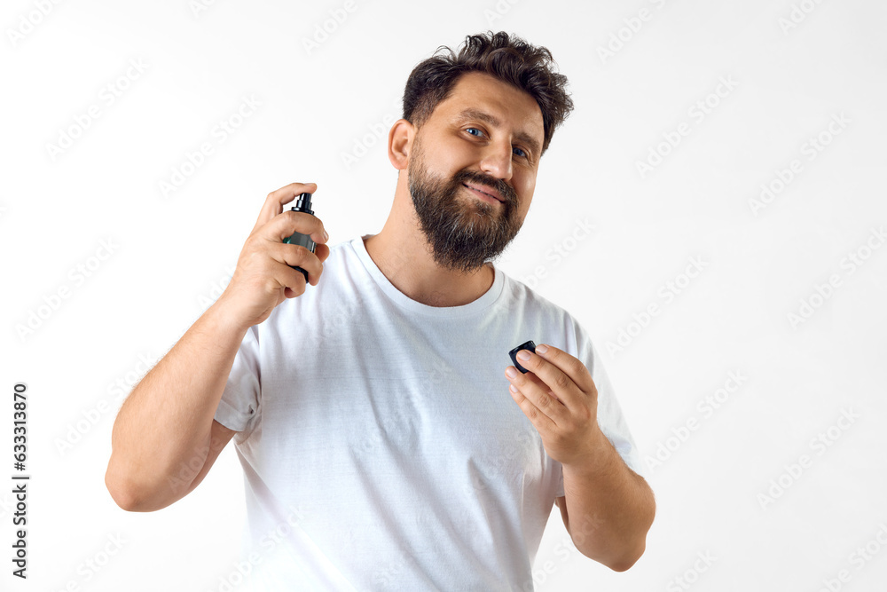 Handsome, mature, bearded man in white t-shirt applying perfume against white studio background. Concept of men's beauty, skin care, cosmetology, health and wellness. Copy space for ad Handsome, mature, bearded man in white t-shirt applying perfume against white studio background. Concept of men's beauty, skin care, cosmetology, health and wellness. Copy space for ad