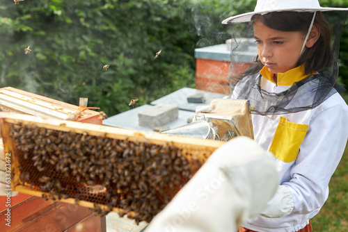 Girl holding smoker near honeycomb frame at beehive