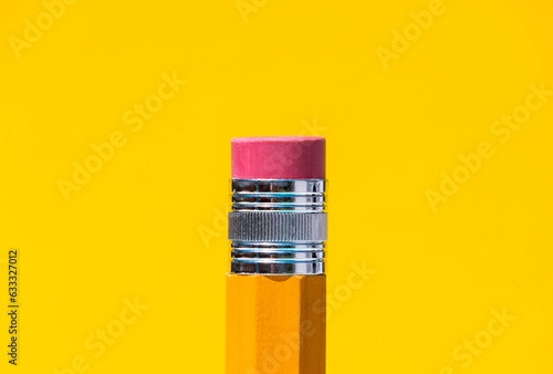 Bright yellow pencil with eraser on top in blue studio photo