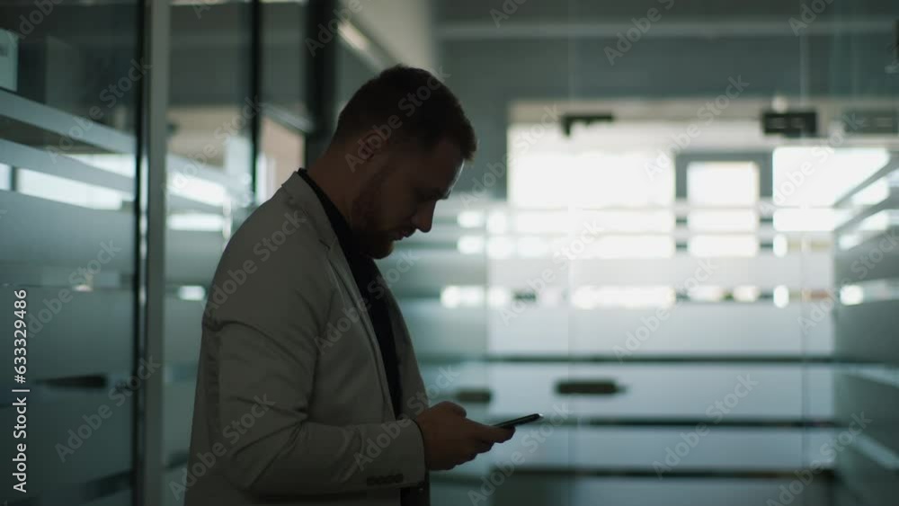 Silhouette of serious businessman in suit dialing number on phone, calling and begin conversation standing in dark hallway corridor of modern business center. Shooting in slow motion. Silhouette of serious businessman in suit dialing number on phone, calling and begin conversation standing in dark hallway corridor of modern business center. Shooting in slow motion.