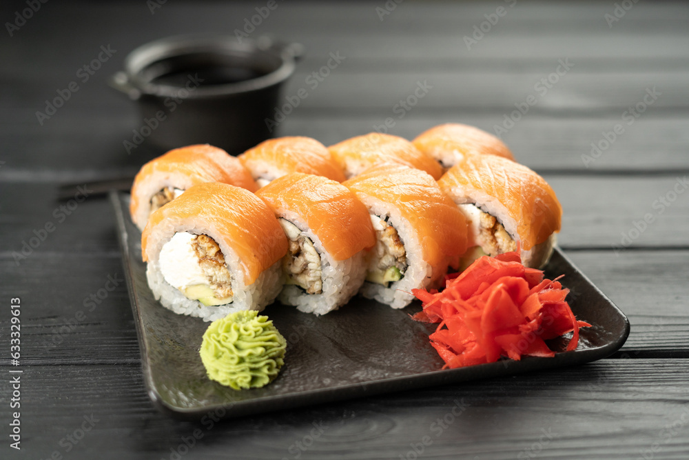 Philadelphia sushi roll with smoked eel, salmon and cream cheese on a wooden table served with soy sauce, wasabi and ginger. Sushi menu. Japanese food. Philadelphia sushi roll with smoked eel, salmon and cream cheese on a wooden table served with soy sauce, wasabi and ginger. Sushi menu. Japanese food.