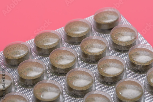 Okrągłe tabletki w opakowaniu z bliska na różowym tle 