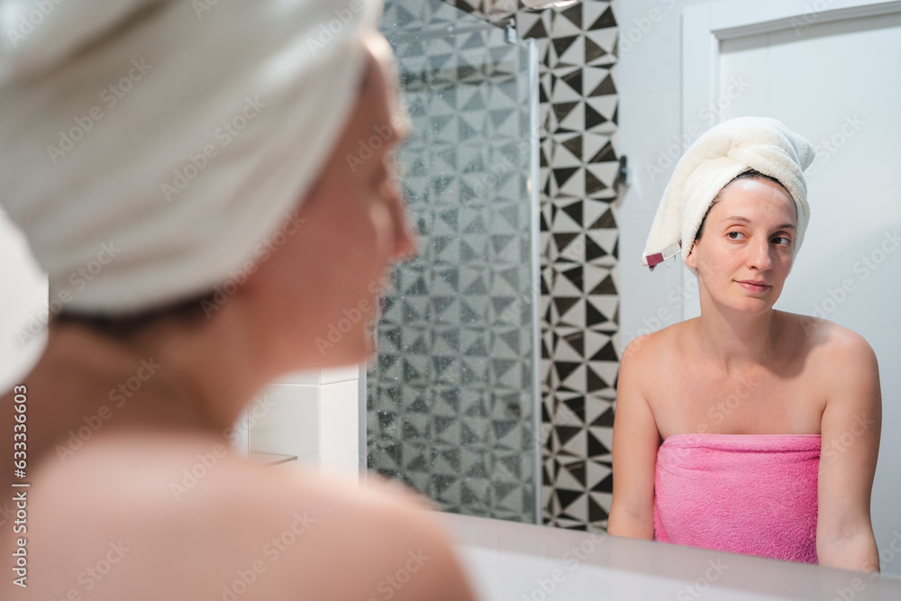 HAPPY PRETTY YOUNG WOMAN TAKING CARE OF HERSELF, PUTTING CREAM ON HER FACE, IN FRONT OF A MIRROR WITH TOWELS COVERING HER HAIR AND BODY HAPPY PRETTY YOUNG WOMAN TAKING CARE OF HERSELF, PUTTING CREAM ON HER FACE, IN FRONT OF A MIRROR WITH TOWELS COVERING HER HAIR AND BODY