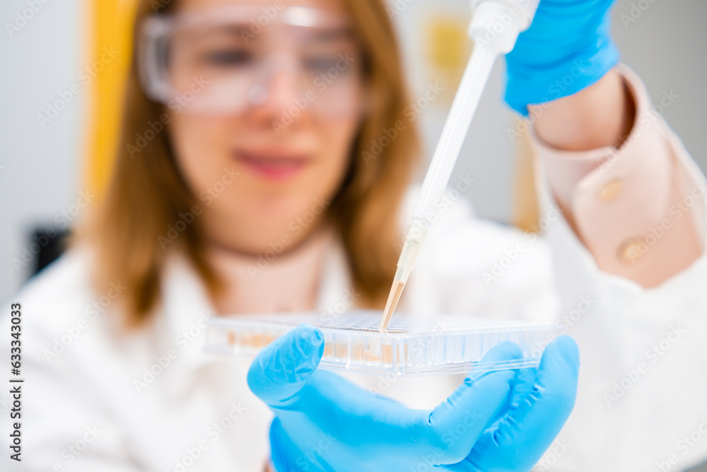 Scientist in goggles and rubber gloves uses pipette for filling 96 well
