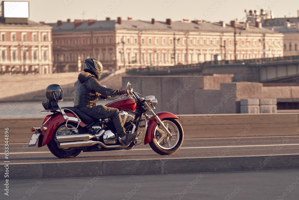 A motorcyclist in a leather jacket rides a red motorcycle on city roads. Biker in a helmet on a chopper travels the country.