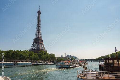 Sunny view of the Eiffel Tower with white boats on the Seine River in Paris at noon. © Aerial Film Studio
