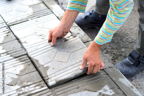 Worker tiler lays tiles with cement outside on summer day. Authentic workflow. Hands with facing tiles.