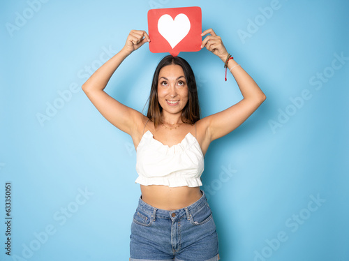 Young happy woman with social media heart Like icon. Indoor studio shot isolated on blue background.