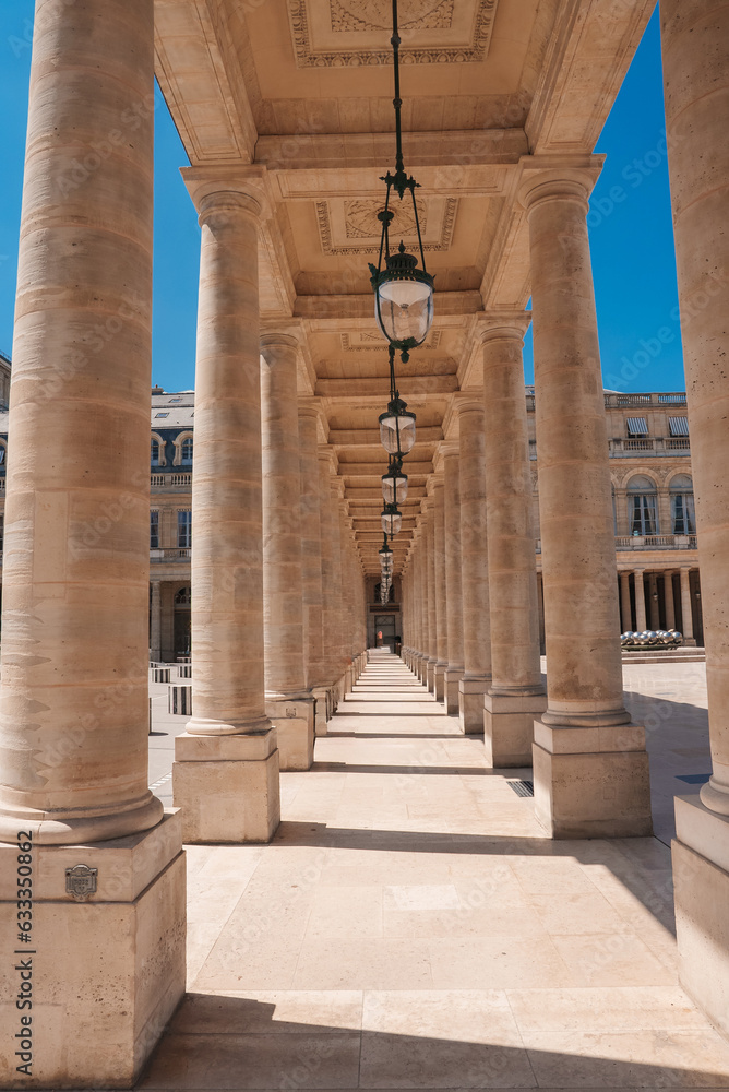 Bright, sunny image of a stone walkway lined with tan neoclassical columns in a building.