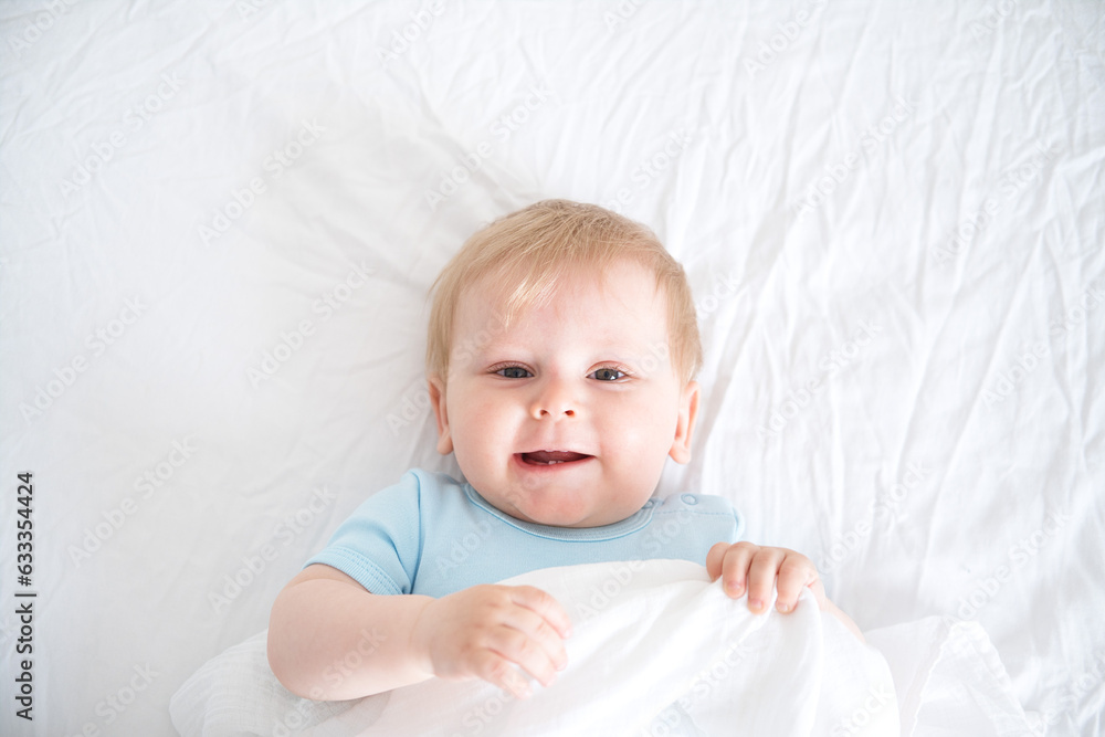A baby with blonde hair smiling laying on a white bed. top view A baby with blonde hair smiling laying on a white bed. top view