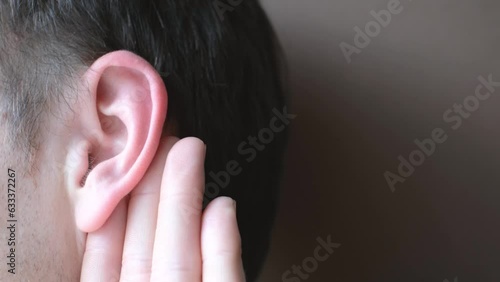 The man listens attentively with her palm to her ear close-up on brown background, news concept. photo