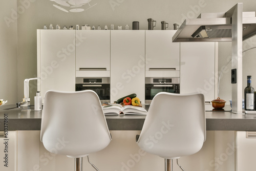 Fototapeta Naklejka Na Ścianę i Meble -  two white chairs in a kitchen with a book on the counter top and an open door leading to another room