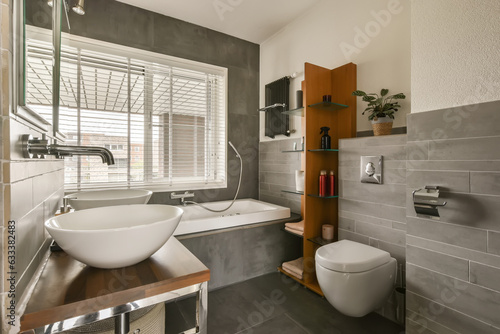 a bathroom with a sink  toilet and window in the back wall is made of dark grey tiles on the floor