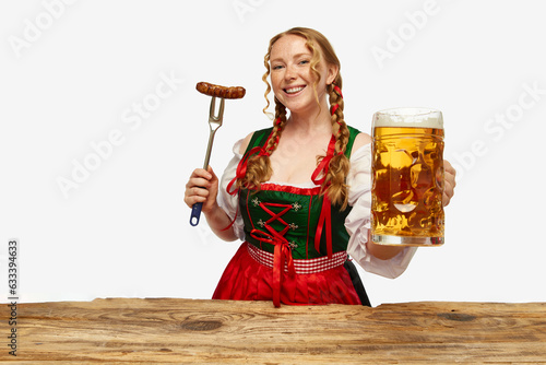 Smiling young redhead woman dressed traditional dirndl, holding huge juicy,appertizing Bavarian sousage and beer mug. Concept of Oktoberfest. photo