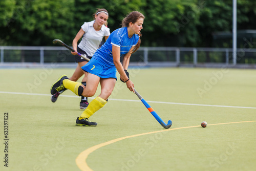 Young female player running with ball in attack on the pitch in field hockey game