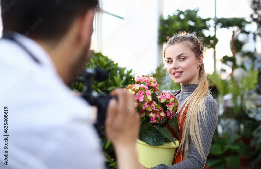 Blogger Woman Recording Pink Flower on Camera. Girl Florist Posing with Colorful Hydrangea Blossom to Man with Camcorder. Domestic Plant Blog. Female Holding Flowerpot with Yellow Hortensia